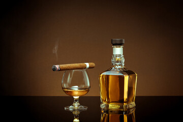 close up view of cigar, bottle of cognac and a glass aside on color back. 