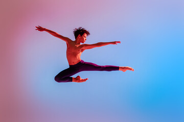 teen ballet boy jumps barefoot under colored light.