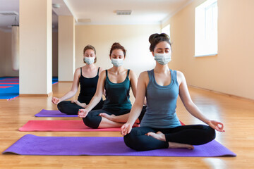 A group of young caucasian women in protective masks do yoga in the studio. The concept of a sporty lifestyle and new normal