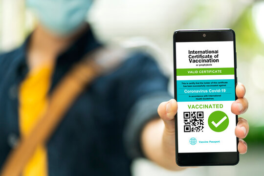 Smartphone displaying a valid digital vaccination certificate passport for COVID-19 in male's hand, public area background. Vaccination, disease immunity passport, health and safty travel concepts