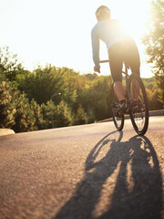 Smooth ride. Rear view of male biker cycling on the road in park on a sunny day