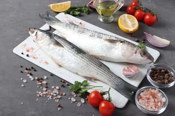 Raw fish mullet with ingredients and seasonings on white plastic board on dark background.