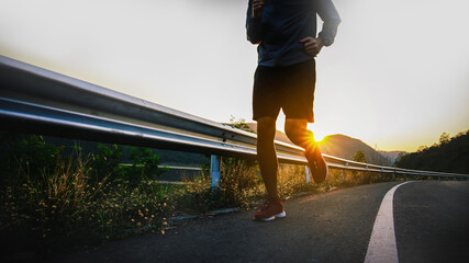 runner training outdoors exercising on asphalt road at sunrise . Fit handsome athlete jogger...