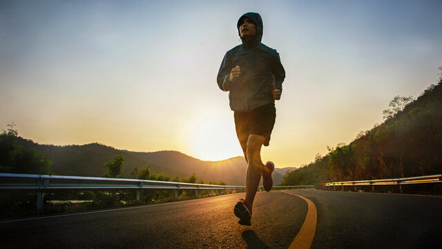 Full length of male runner training outdoors exercising on asphalt road at sunrise . Fit handsome athlete jogger working out for marathon run outside in summer - Powered by Adobe
