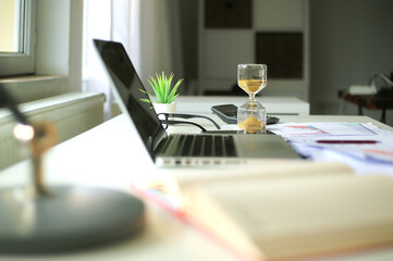 Hourglass and computer standing on graph or analytical papers, business equipment.