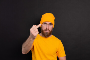 Portrait of bearded european man in yellow hat on black background serious look shows middle finger look to camera