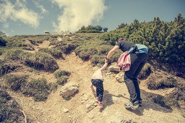Rear view of mother and daughter tackling steep slope in mountains.