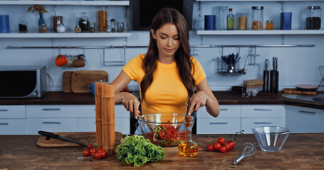 young woman mixing fresh salad in kitchen