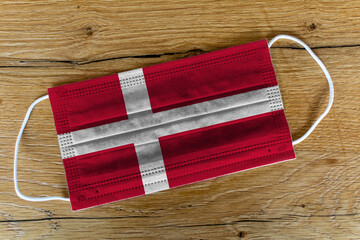 Fototapeta na wymiar A surgical face mask with the painted flag of Danmark on a wooden background. Concept of Danmark during a pandemic, Covid-19, Coronavirus.