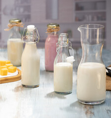 Bottles of milk and yogurt on a wooden table with cheese plater on a grey background