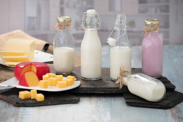 Bottles of milk and yogurt on a wooden table with cheese plater on a grey background