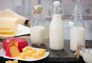 Bottles of milk and yogurt on a wooden table with cheese plater on a grey background