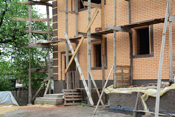 Fototapeta na wymiar A view of a new brick house under construction with scaffolding, uninstalled windows and unfinished porch. Clean construction site.