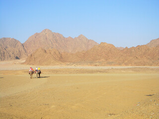 Fototapeta na wymiar Camel travelers, camel ride on a desert safari in Egypt. Beautiful Egypt's desert landscape with camel riders.