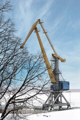 Fototapeta na wymiar High port crane stands in the snow against the blue sky