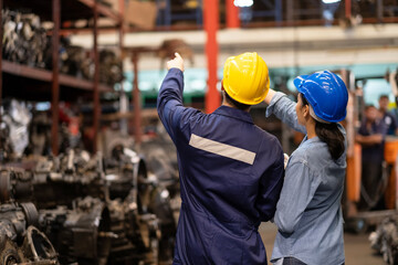 Two engineer or manager worker wearing safety helmet standing in the automotive part warehouse. Man and woman point forward to spare part in the rack. Inspector and quality check concept.