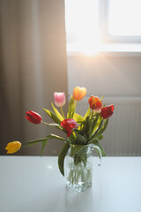 Bunch of fresh cut tulips in vase on a table with soft focus and bright light from the window
