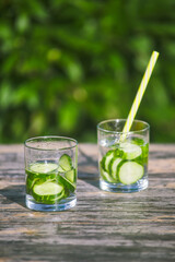 two freshly prepared summer cocktails in a glass. cold drinking cucumber water on a hot sunny day in nature. vertical frame