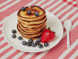 Close-up of delicious pancakes, with fresh blueberries, strawberries and maple syrup on a light background. With space to copy. Sweet maple syrup flows from a stack of pancakes
