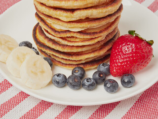 Close-up of delicious pancakes, with fresh blueberries, strawberries and maple syrup on a light background. With space to copy. Sweet maple syrup flows from a stack of pancakes
