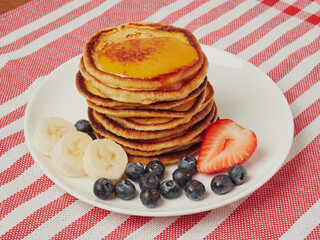 Close-up of delicious pancakes, with fresh blueberries, strawberries and maple syrup on a light background. With space to copy. Sweet maple syrup flows from a stack of pancakes