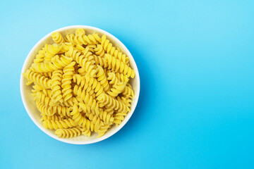 Fusilli italian pasta in white ceramical bowl on blue background with space for text, top view.