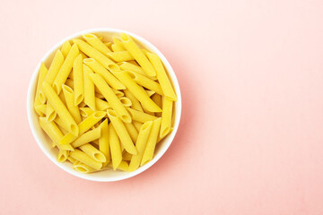 Penne italian pasta in white ceramical bowl on pink background with copy space, top view.