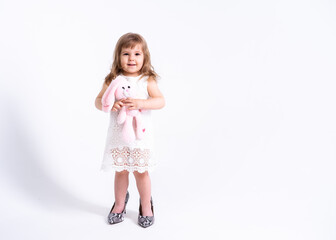 Funny little girl in white dress trying her mother shoes with heels on white background