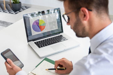 Businessman sitting at desk and using mobile phone and laptop while working in the office