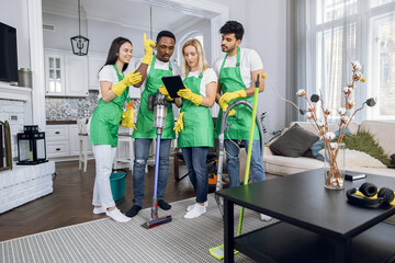 Purposeful high skilled multiracial cleaning team checking their responsibilities on tablet pc, starting to clean customer's house. Cleaning service concept