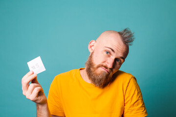 Bearded european man in yellow shirt isolated on turquoise background holding yes with surprise and...
