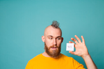 Bearded european man in yellow shirt isolated on turquoise background holding yes with surprise and...