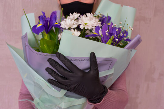 A Woman In A Black Pitta Mask And Black Gloves Holds A Beautiful Bouquet Of White And Purple Spring Flowers In Her Hands.