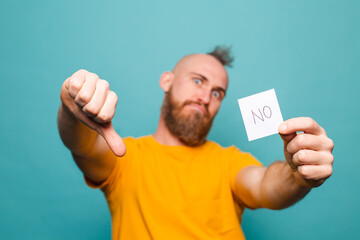 Bearded european man in yellow shirt isolated on turquoise background holding no strong man serious face