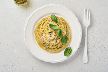 Pasta spaghetti with pesto sauce and fresh basil leaves in white bowl. Grey background. Mock up. Top view.