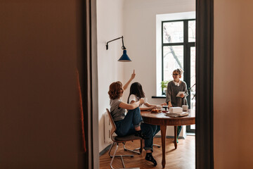 Gorgeous girls sitting at table and laughing in good day. Indoor shot of good-humoured friends spending time at home.