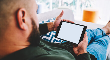 Crop bearded man with tablet relaxing in cozy room