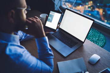 Crop male entrepreneur working with gadgets in office at dusk