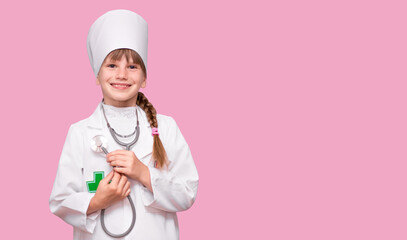 Little, cute girl future doctor dressed white medical apron with stethoscope isolated on pink background, copy space