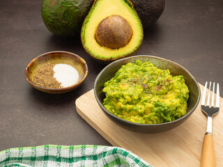 Fresh guacamole on a dish placed on a cutting wooden board with ingredients for homemade guacamole avocados, lemon, salt, and pepper. Top view.  Concept of traditional Mexican preparation