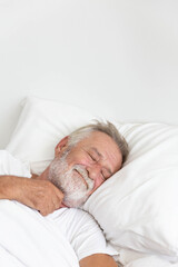 Senior retirement man sleeping happily in his white blanket bed in bedroom