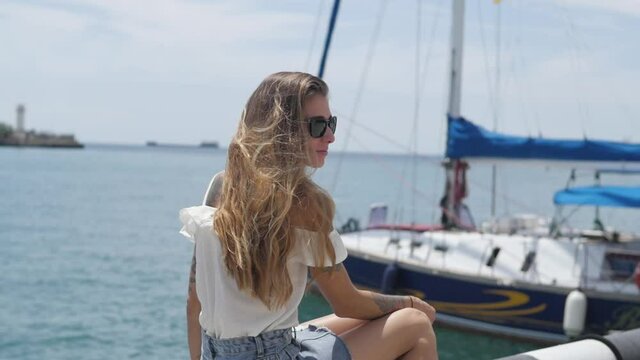 Blond woman in sun glasses looking at beautiful sea bay celebrating scenic landscape enjoying vacation travel adventure nature. young woman on the background of the yacht