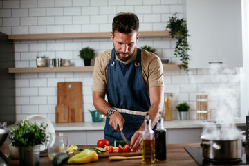 Young man preparing vegetable salad in the kitchen. Happy man making healthy meal.