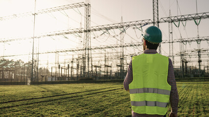 Electrical engineer wearing a helmet and safety vest working with tablet near high voltage...