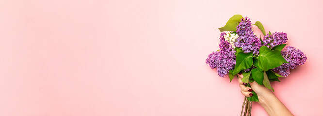 Woman holding beautiful bouquet of lilac flowers on soft pastel pink background with copy space.