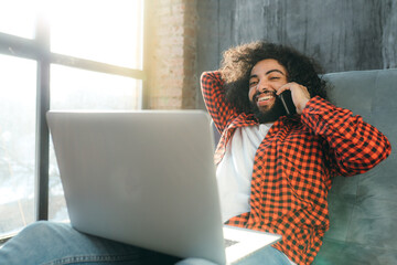 African american businessman sitting in a chair working at a laptop and talking on the phone