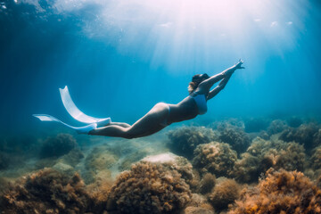 Freediver glides over sandy sea with white fins. Slim woman free diver in ocean