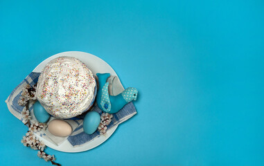 Obraz na płótnie Canvas Easter composition. Eggs, apricot flowers, a cute handmade bird and a glazed Easter cake decorated with sugar sprinkles on a blue background. Happy Easter Holidays. Top view. Free space.