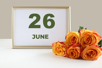 day of the month 26 June calendar photo frame and yellow rose on a white table
