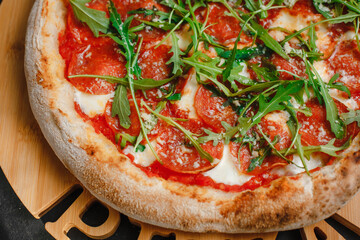 Homemade Pepperoni pizza with Mozzarella cheese, salami, tomato sauce, pepper, arugula and spices. Italian pizza on a dark gray black background